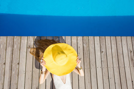Playful woman lying with yellow sunhat on the poolside. Summer vacation concept