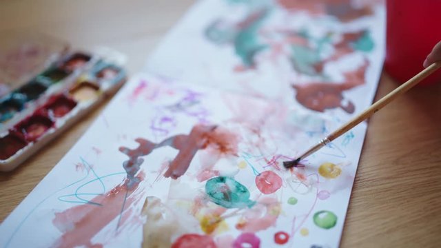 Hands of little girls painting with watercolors in album on the floor.