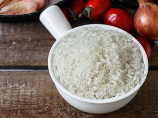 rice round-grained raw on a wooden surface with tomatoes, onions, shrimps
