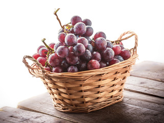 Red grapes branch in knitted basket on wooden old rustic table and white background in studio