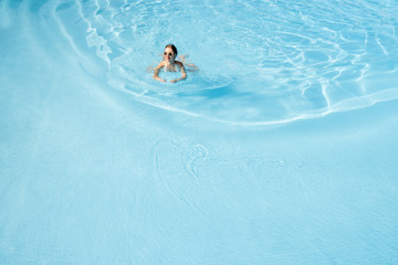 Young woman in swimsuit swimming at the basin with blue water. General view from above