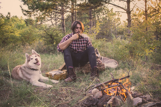 Folk or country guitar player in the forest with dog, man in woods, campfire and sunset background 