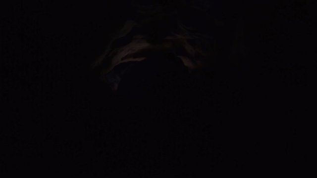 Young man with hard effort stretches out his hand trying take flashlight which lies on the ground in cave. Absolutely deep darkness around. Traveler inside the cave.