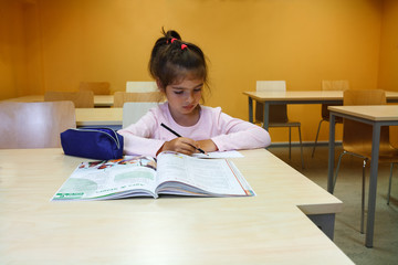 A girl is in the class and learning to read and to write with a pencil, she is writing with a pen in her notebook