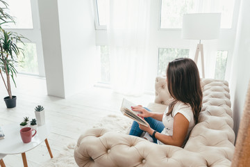 Young pretty woman sitting on the sofa and reading a book enjoys of rest