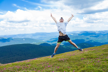 Happy handsome man tourist jump high into the sky for joy during the walk in beautiful mountains