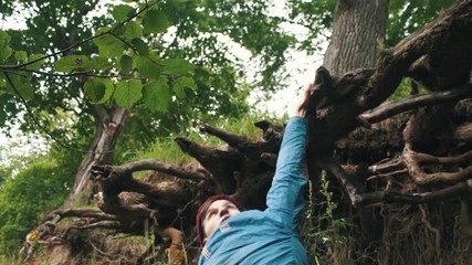 Young courageous traveler climbing up top by slope clinging to the roots of trees. Freedom travel adventure theme