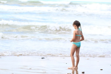 Fototapeta na wymiar The small beautiful girl with plaits in a turquoise bathing suit on seacoast