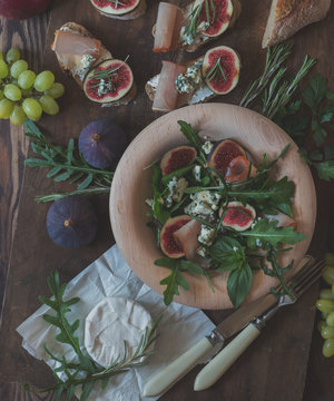 Easy diet salad with arugula, figs and blue cheese on a brown wooden surface. Sandwiches with ricotta, fresh figs, prosciutto, rosemary and blue cheese. Delicious fruity breakfast, top view. Toned
