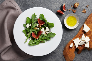 Seasonal salad with figs, arugula, walnuts and feta cheese on textured stone background