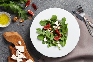 Seasonal salad with figs, arugula, walnuts and feta cheese on textured stone background