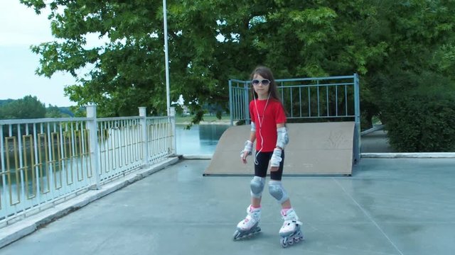 A little girl in sunglasses rolls on rollers. A happy girl in headphones skates on roller skates.