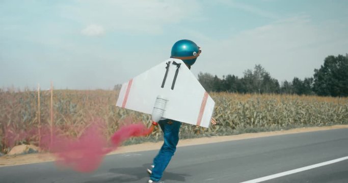 TRACKING Little boy wearing helmet and styrofoam wings running on a rural road, pretending to be a pilot. 4K UHD RAW edited footage