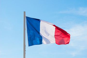 French flag fluttering in a brisk breeze against a bright blue sky in summer background.