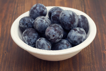 fresh plums in white bowl on wooden background