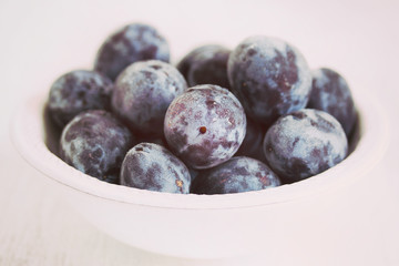 fresh plums in white bowl on wooden background