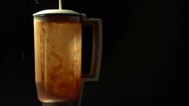 In the blender, crush the red tomatoes, then add a white sauce, prepare the liquid seasoning against a black background, slow motion.