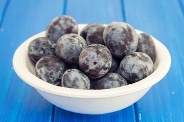 fresh plums in white bowl on blue wooden background