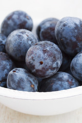 fresh plums in white bowl on wooden background