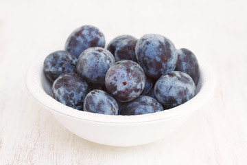 fresh plums in white bowl on wooden background