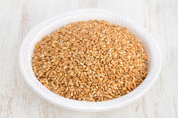 uncooked spelt on white plate on wooden background
