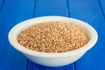 uncooked spelt on white plate on wooden background