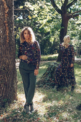 Fashion portrait of two happy woman in trendy dress posing in a public garden. Girl with long healthy hair and beautiful smile.