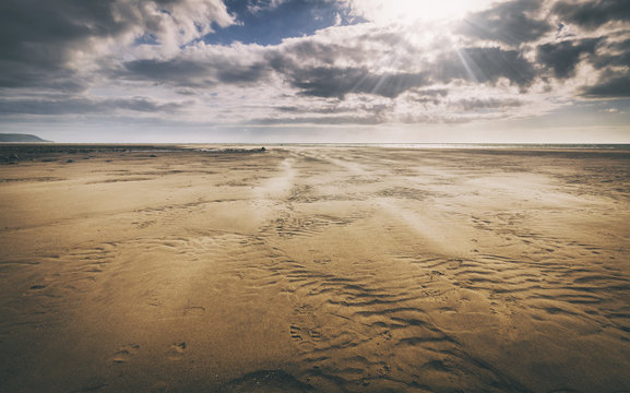 Scenic Coastal Scape with Wind Patterns on Sand and Sunrays Through Clouds