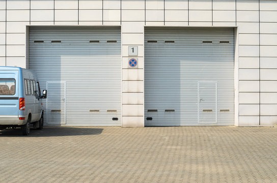 Two gray garage doors and a parked minibus. Large automatic up and over garage doors with inclusion of smaller personal door.