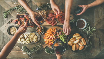Flat-lay of friends hands eating and drinking together. Top view of people having party, gathering, celebrating together at wooden rustic table set with different wine snacks and fingerfoods