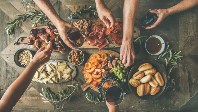 Fototapeta Flat-lay of friends hands eating and drinking together. Top view of people having party, gathering, celebrating together at wooden rustic table set with different wine snacks and fingerfoods