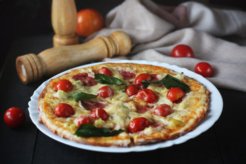 Hot pizza slice with melting cheese on a dark wooden table with tomatos.Gray drape.