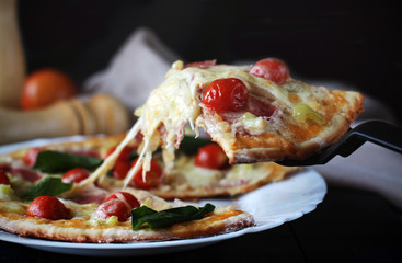 Hot pizza slice with melting cheese on a dark wooden table with tomatos.Gray drape.