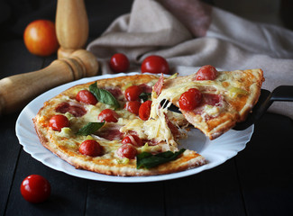 Hot pizza slice with melting cheese on a dark wooden table with tomatos.Gray drape.
