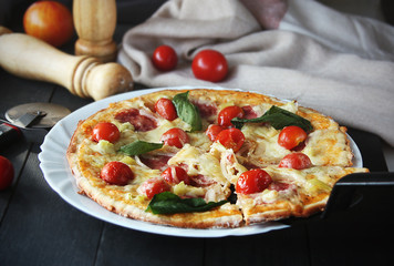Hot pizza slice with melting cheese on a dark wooden table with tomatos.Gray drape.