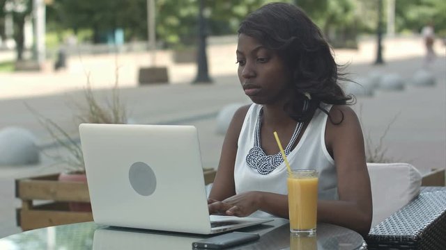 African american woman working on laptop outdoor and drinking juce