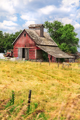 Old red barn on a farm with grassy pasture in the foreground and grees and sky in the background