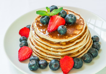 American pancakes with blueberries, strawberries, and honey against white background