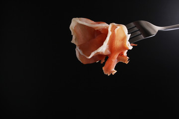 prosciutto, jamon on a fork a dark background