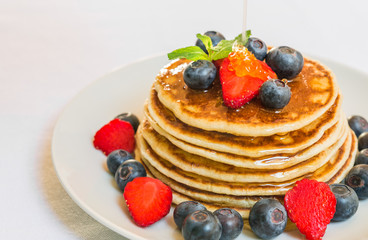 American pancakes with blueberries, strawberries, and honey against white background