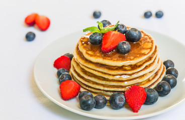 American pancakes with blueberries, strawberries, and honey against white background