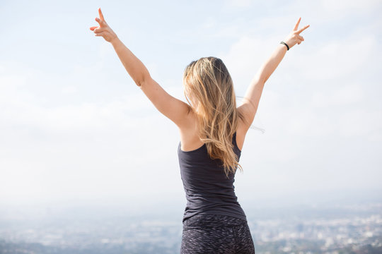 Slender girl standing on the top of the hill showing victory signs with her fingers