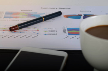 Workplace with charts, phone, coffee cup,  on wooden table.