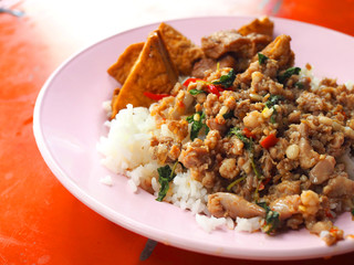 Close up perspective of Thai local traditional street food stall: stir fried spicy minced pork with holy basil, big chunk of deep fried tofu boiled in black sweet brown Chinese sauce, topped on rice