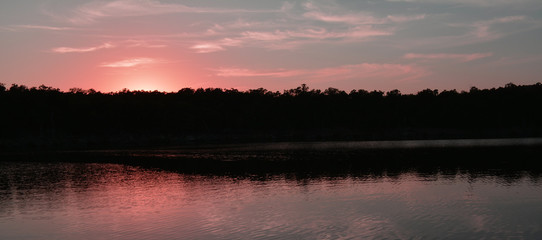 Naklejka premium Lake Sunset/PInk sunset reflection over a lake and trees.