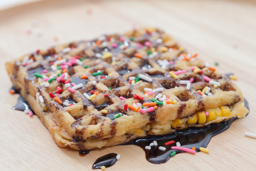 Waffles with melted chocolate and colorful sparkle on wooden plate