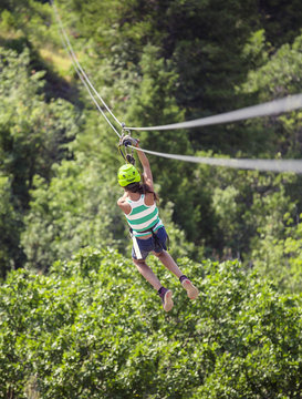 Teen girl riding a zip line through the forest. View from behind 