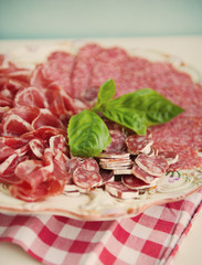 Cold smoked meat plate with pork chops, prosciutto, salami and bread sticks on white wooden background. From top view
