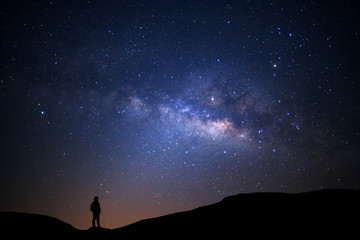 Obraz premium Krajobraz z drogą mleczną, nocne niebo z gwiazdami i sylwetka człowieka stojącego na wysokiej górze
