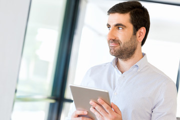 Fototapeta premium Young handsome businessman using his touchpad standing in office